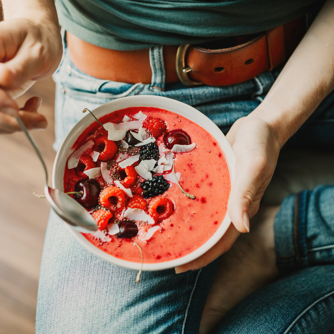 Woman sat down eating a berry smoothie bowl