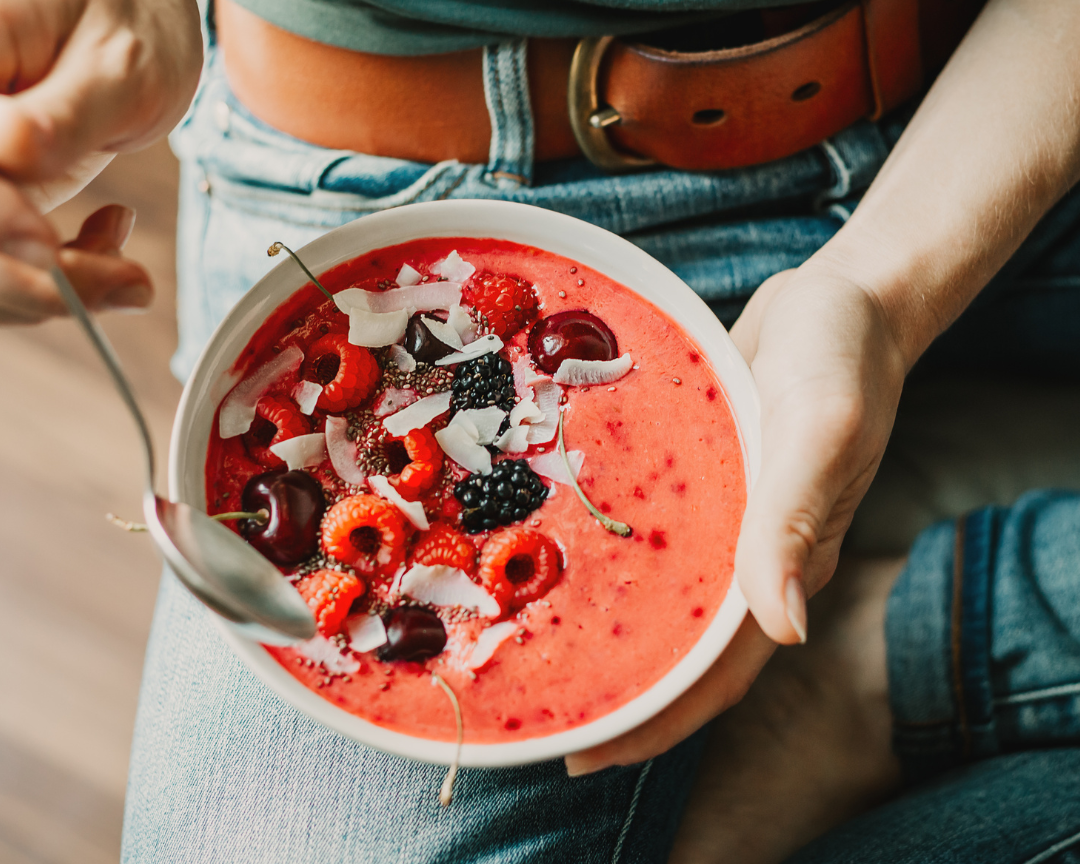 Woman sat down eating a berry smoothie bowl