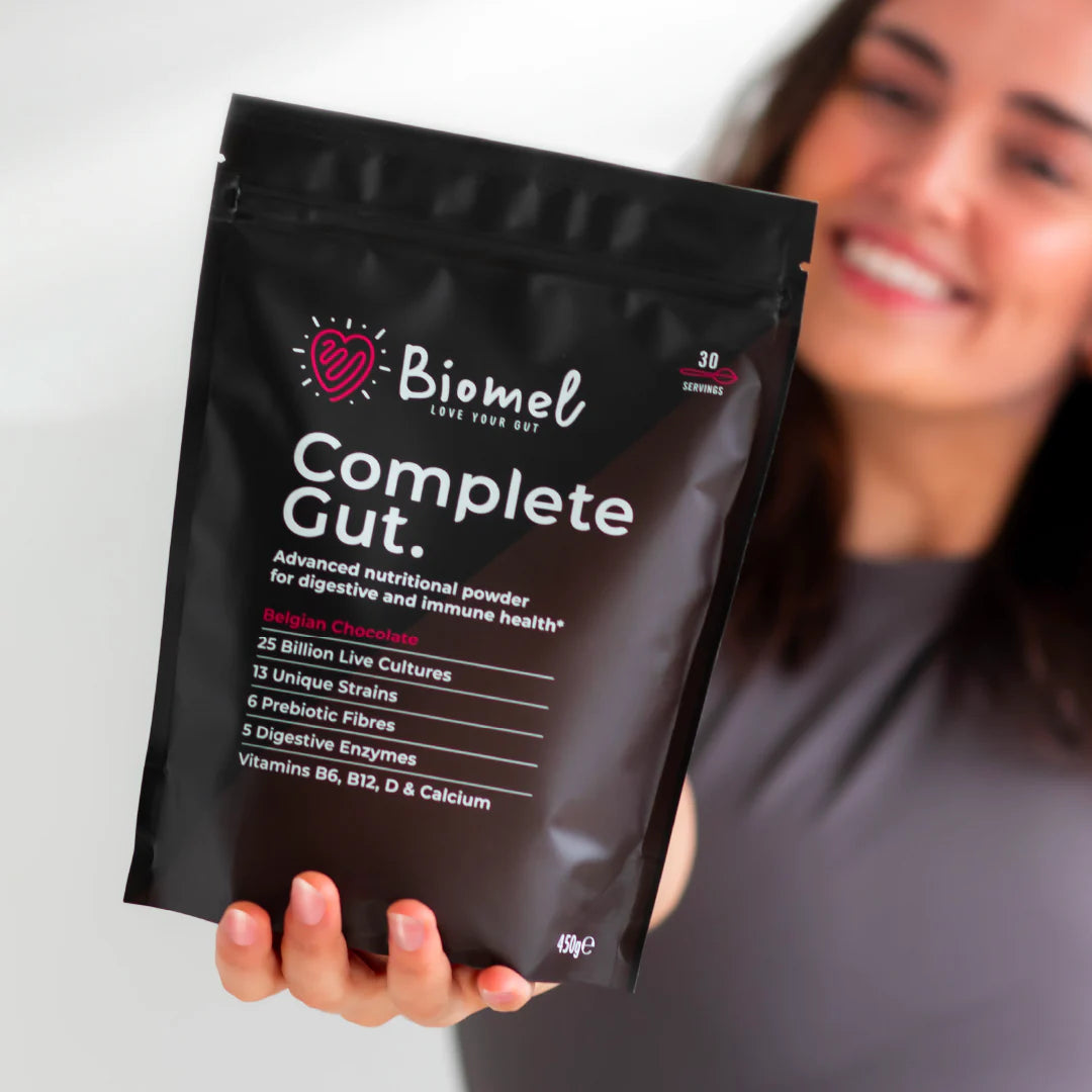  A person holding a packet of "Biomel Complete Gut" nutritional powder, featuring details like "25 Billion Live Cultures," "13 Unique Strains," and "Belgian Chocolate" flavour.