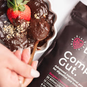 Hand holding chocolate mixture with strawberry & nuts, "Belgian Chocolate Complete Gut" packet in background.